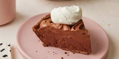 a piece of chocolate pie with whipped cream on top sits on a pink plate next to a cup