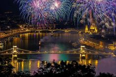 fireworks are lit up in the night sky over a river and bridge with lights on it