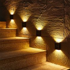 some lights that are on the side of some steps in front of a stone wall