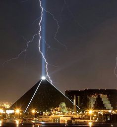 lightning strikes over the pyramid at night with buildings in the foreground and city lights behind it