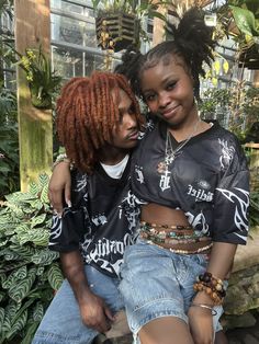 two young women sitting next to each other in front of plants and greenery, one with red dreadlocks on her head