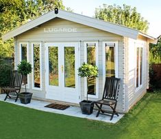 a small white shed with two chairs and potted plants on the front porch area