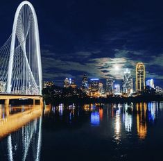 a bridge that is over some water with the city lights in the background at night