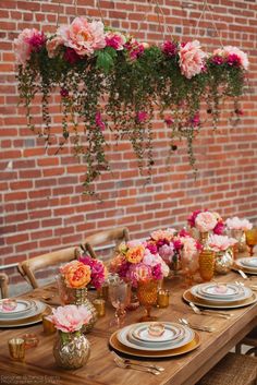 the table is set with plates and flowers hanging from the brick wall behind it, along with other place settings