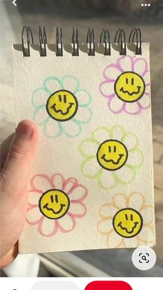 a hand holding up a small notebook with smiley faces on it