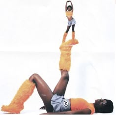 a woman in an orange outfit is doing a handstand while holding a doll