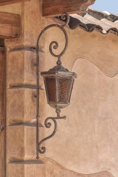 an old fashioned street light hanging from the side of a building with stucco and wood