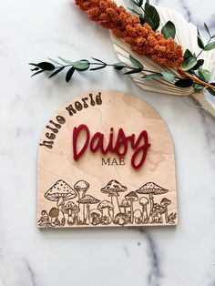 a wooden sign that says, hello world daisy made with mushrooms and leaves on it