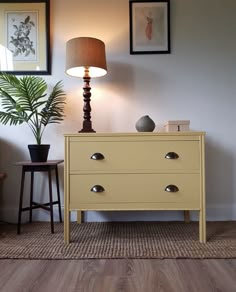 a yellow dresser sitting next to a lamp on top of a wooden table in a living room