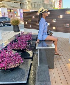 a woman sitting on top of a bench next to purple flowers