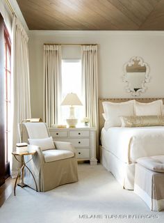 a bedroom with a bed, chair and mirror on the wall next to two windows