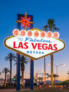 the famous las vegas sign is lit up at night with palm trees and buildings in the background