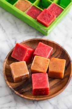 several cubes of soap on a wooden plate next to green trays with red and orange squares