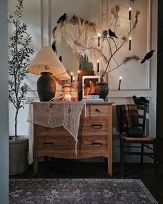 a room with a dresser, table lamp and pictures on the wall above it is decorated with branches