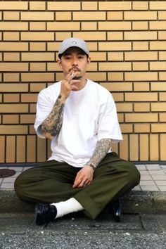 a man sitting on the ground with his hand in his mouth and wearing a baseball cap