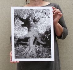 a woman holding up a black and white photo of a large tree in the woods