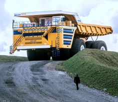 a large yellow dump truck parked on top of a dirt road next to a hill