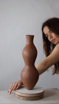 a woman touching a vase on top of a table