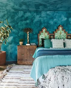 a bedroom decorated in teal and green with a bed, rugs, potted plants and wicker furniture