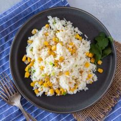 rice with corn and cilantro on a black plate next to a blue towel