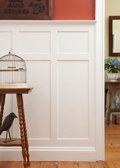 a bird in a cage sitting on top of a wooden table next to a white wall