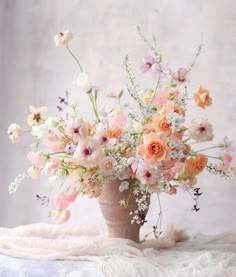 a vase filled with lots of flowers on top of a white cloth covered tablecloth