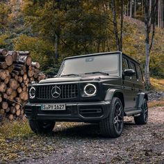 a black mercedes g - class is parked in front of some logs