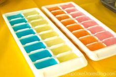 two ice trays filled with different colored popsicles on top of a yellow table