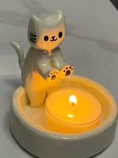 a cat figurine sitting on top of a bowl with a lit candle in it