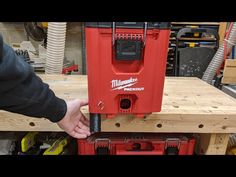 a red milwaukee tool box being held by a man's hand over a workbench