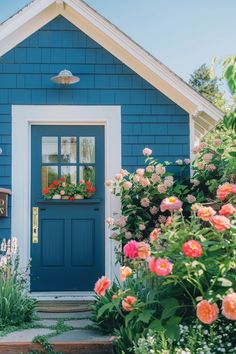 a blue house with white trim and flowers on the front door is surrounded by greenery