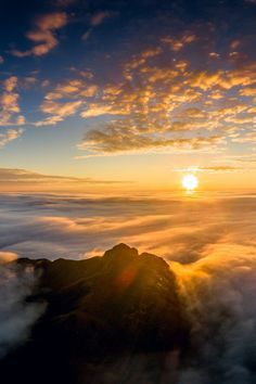 the sun is setting over some clouds in the sky, with mountains and hills below