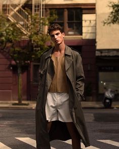 a man is standing in the middle of an intersection wearing shorts and a trench coat