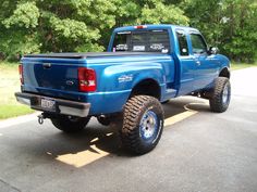 a blue pick up truck parked on the side of a road with trees in the background