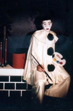 a man dressed in white sitting on top of a brick wall holding a paintbrush