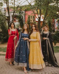 three women in long dresses standing next to each other on a brick floored walkway