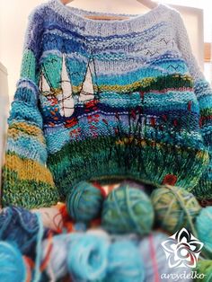 there is a sweater that has been knitted and sits on top of yarn balls