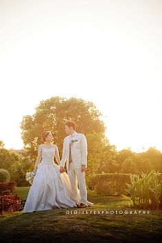 the bride and groom are walking together in their wedding attire at sunset, holding hands