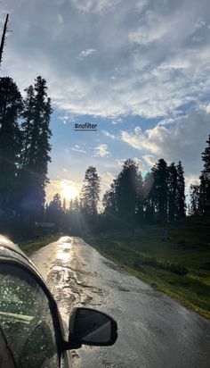 the sun is shining through the clouds over a road with trees and grass on both sides