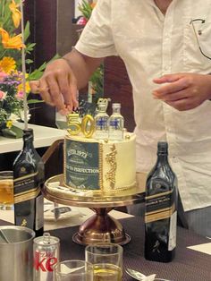 a man cutting into a cake on top of a table with wine bottles and glasses