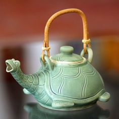 a green teapot with a bamboo handle sitting on top of a table