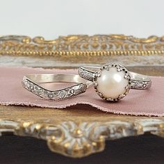 Timeless and classic, this vintage inspired pearl engagement ring and curved wedding band set are reminiscent of the Edwardian era when fine metalwork was designed with intricate details and delicate settings that were fashioned to resemble the patterns of fine lace. The vintage style Edwardian-inspired pearl ring is handcrafted from recycled sterling silver where a lightly oxidized floral band is set with a luminous 8-8.5mm cultured creamy white freshwater pearl in a filigree heart-crown settin Classic Silver Stackable Rings With Rose Cut Diamonds, Elegant Silver Stackable Rings With Rose Cut Diamonds, Elegant Wedding Jewelry With Milgrain Detail, Elegant Silver Bridal Set With Intricate Design, Elegant Silver Bridal Sets With Round Band, Classic Pearl Ring For Wedding, Elegant Round Band Bridal Sets For Wedding, Classic Wedding Pearl Ring, Elegant Bridal Sets With Round Band For Wedding