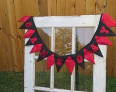 a red and black banner is hanging on a window sill in front of a wooden fence