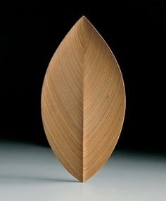 a wooden leaf shaped object sitting on top of a white table next to a black wall