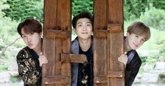 two young men standing next to each other in front of a wooden structure with trees behind them