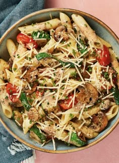 a bowl filled with pasta and vegetables on top of a pink table next to a pair of blue jeans