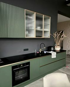 a modern kitchen with green cabinets and black counter tops is pictured in this image, there is a white chair next to the sink