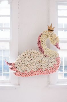 a swan made out of flowers sitting on top of a white wall next to two windows