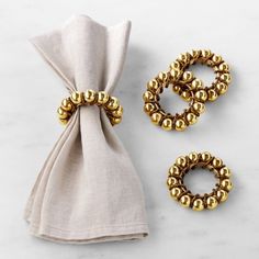 two napkins with gold beads on them next to a napkin holder and napkin ring