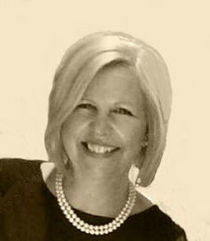 a black and white photo of a woman with blonde hair wearing a pearl necklace smiling at the camera